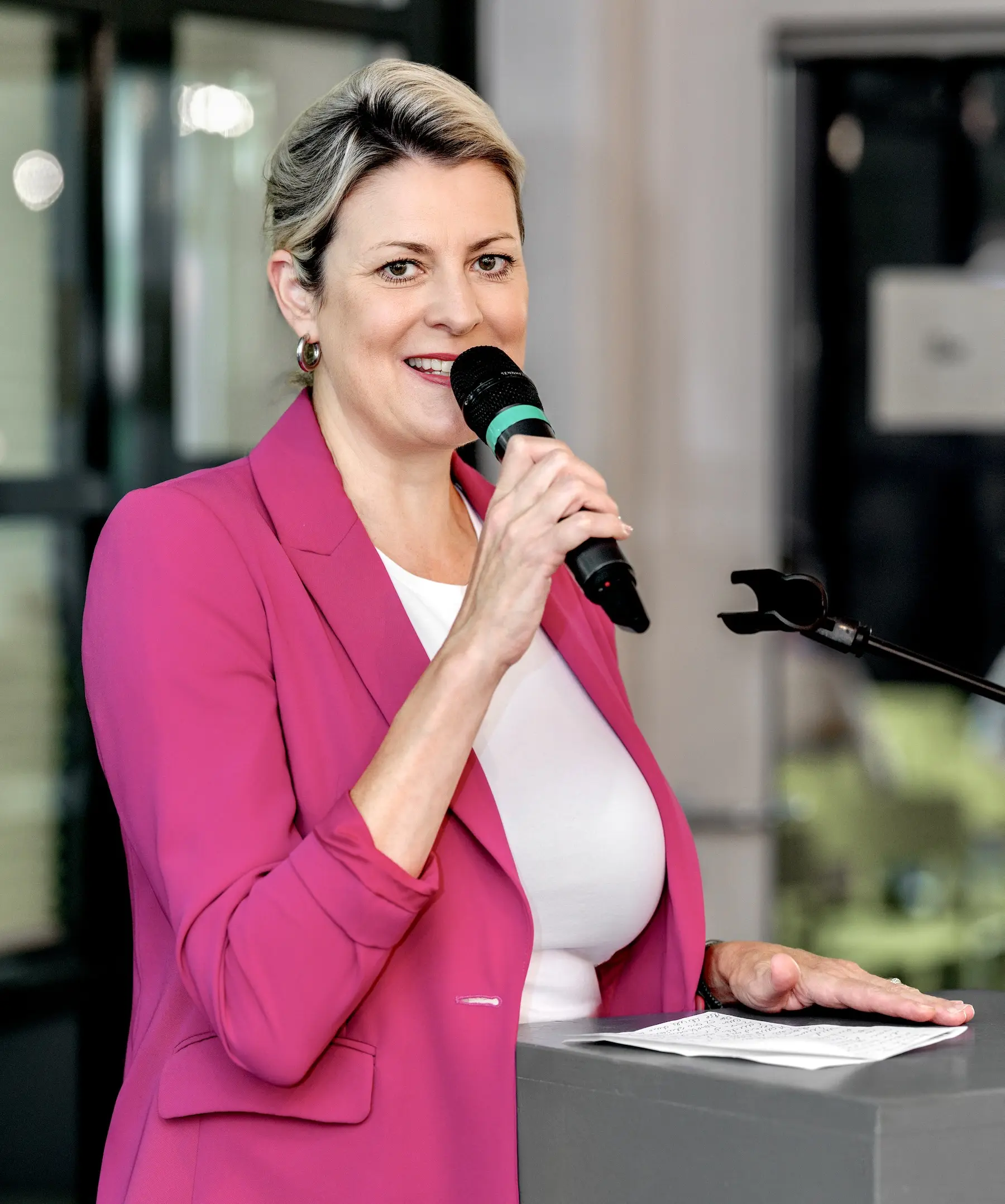 Rednerin im pinken Blazer spricht mit einem Mikrofon zu den Gästen